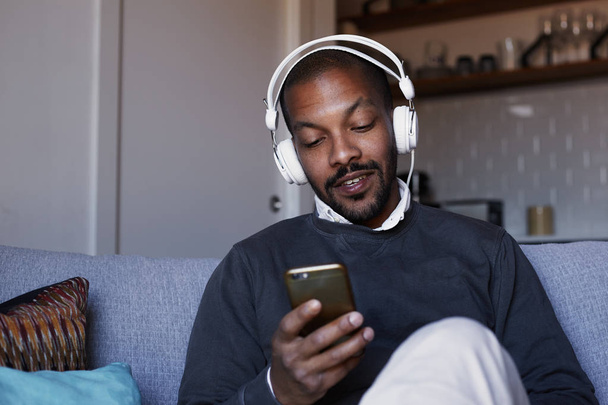Attractive African American man with white headphones listening to music on his phone. Concept of relaxation. - Zdjęcie, obraz