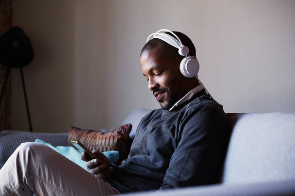 Attractive African American man with white headphones listening to music on his phone. Concept of relaxation. - Fotó, kép