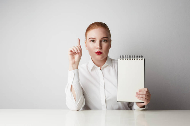 Redhead business woman posing in shirt holding empty notepad over white background. - Foto, imagen