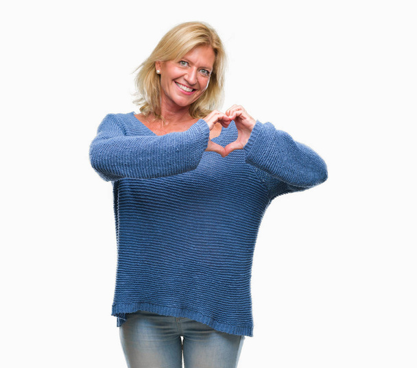 Mujer rubia de mediana edad con suéter de invierno sobre fondo aislado sonriendo en el amor mostrando el símbolo del corazón y la forma con las manos. Concepto romántico
. - Foto, Imagen