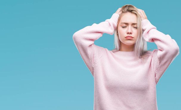 Giovane donna bionda che indossa maglione invernale su sfondo isolato che soffre di mal di testa disperato e stressato perché il dolore e l'emicrania. Mani sopra la testa
. - Foto, immagini