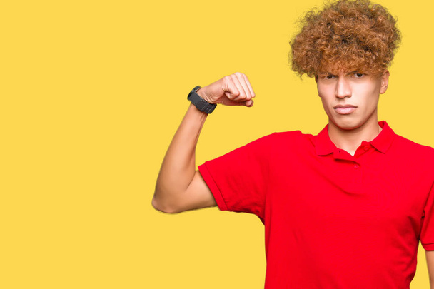 Homem bonito novo com cabelo afro vestindo t-shirt vermelha Pessoa forte mostrando o músculo do braço, confiante e orgulhoso do poder
 - Foto, Imagem