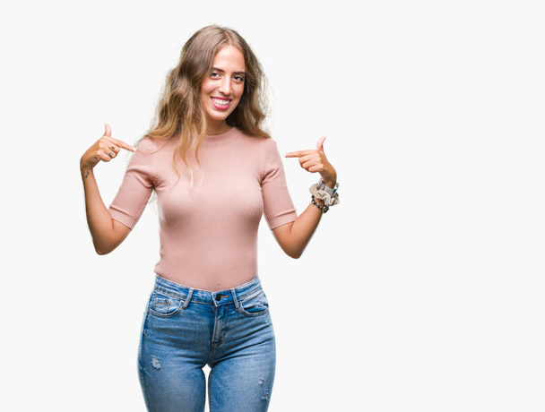 Beautiful young blonde woman over isolated background looking confident with smile on face, pointing oneself with fingers proud and happy. - Foto, imagen