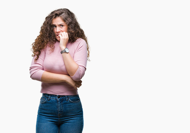 Beautiful brunette curly hair young girl wearing pink sweater over isolated background looking stressed and nervous with hands on mouth biting nails. Anxiety problem. - Photo, Image