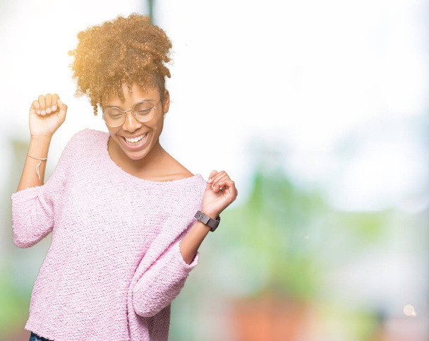 Beautiful young african american woman wearing glasses over isolated background Dancing happy and cheerful, smiling moving casual and confident listening to music - Valokuva, kuva