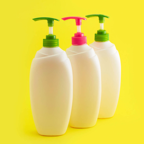 Three plastic bottles with dispenser on yellow background. - Фото, изображение