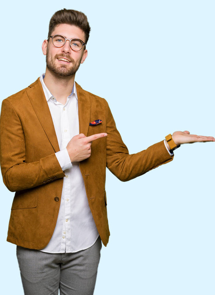 Mladý pohledný obchodní muž nosí brýle ohromil a usmívá se na kameru při prezentaci s ruku a ukazoval prstem. - Fotografie, Obrázek