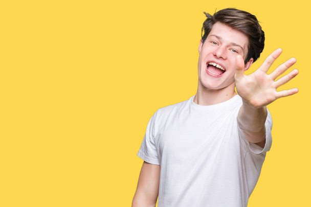 Jonge knappe man dragen casual wit t-shirt over geïsoleerde achtergrond weergeven en met de vingers omhoog nummer vijf terwijl lacht zelfverzekerd en blij. - Foto, afbeelding