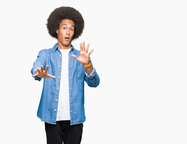 Jonge Afro-Amerikaanse man met afro haar bang en doodsbang met angst expressie stop gebaar met handen, schreeuwen in een roes. Paniek concept. - Foto, afbeelding