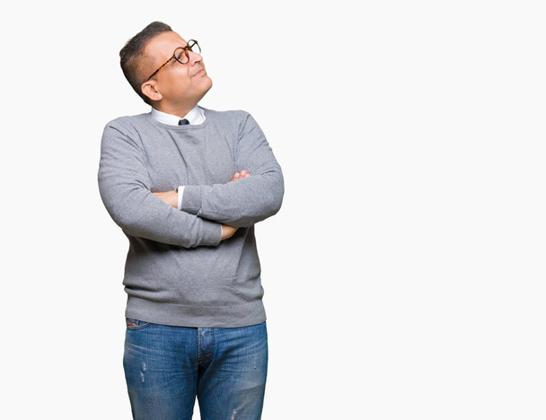 Middle age bussines arab man wearing glasses over isolated background smiling looking to the side with arms crossed convinced and confident - 写真・画像