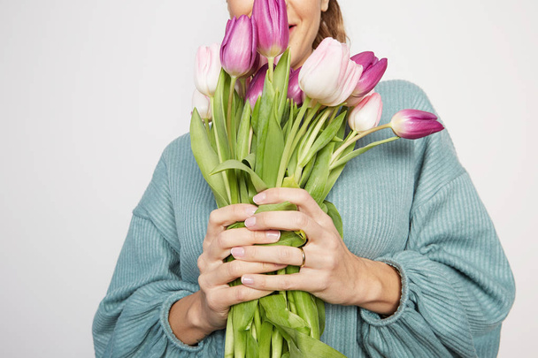 Beautiful woman with big bouquet flowers tulips holding in hands on a light background - Foto, immagini