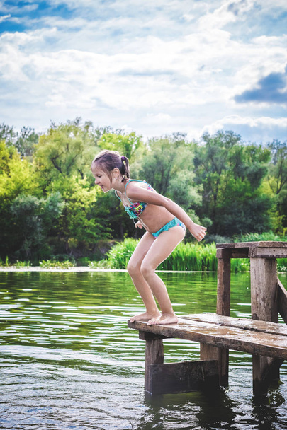 Little cute girl jumping off the dock into a beautiful river at  - Photo, Image