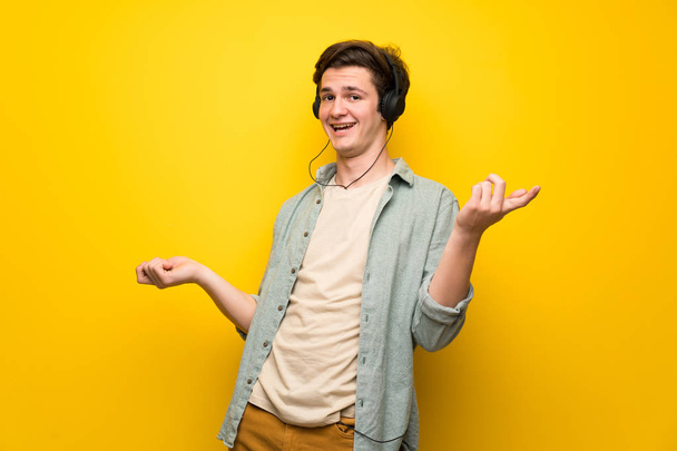 Adolescente hombre sobre la pared amarilla disfrutar bailando mientras escucha música en una fiesta
 - Foto, Imagen