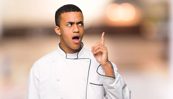 Nuori afro amerikkalainen kokki mies ajatteli idea osoittaa sormella epämääräinen tausta
 - Valokuva, kuva