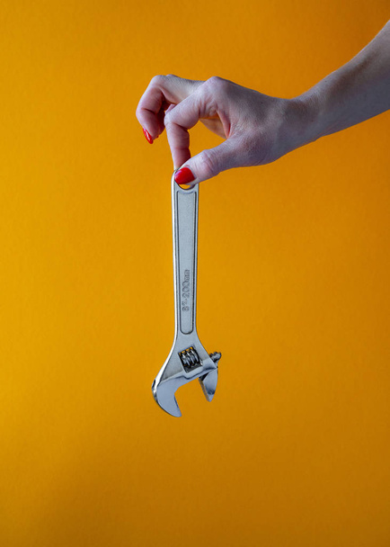 hand of a young woman holding a chrome key, red nail polish, close-up on a yellow background, vertical shot - Фото, изображение