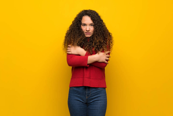 Teenager girl with red sweater over yellow wall freezing - Foto, Imagen