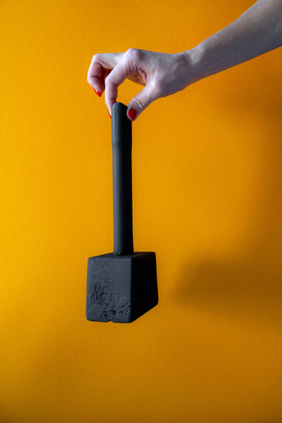 mano di una giovane donna che tiene un martello di legno nero, unghie ricoperte di vernice rossa, sfondo giallo brillante, primo piano, colpo verticale
 - Foto, immagini