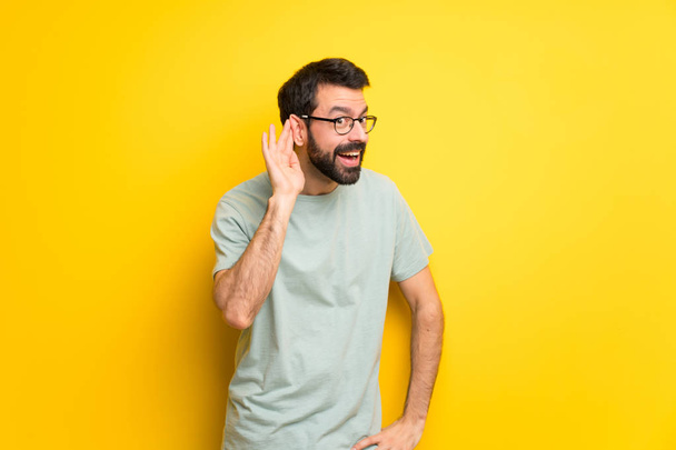 Man with beard and green shirt listening to something by putting hand on the ear - Fotografie, Obrázek