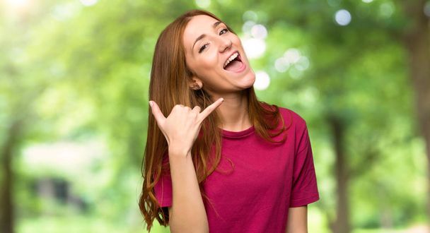Young redhead girl making phone gesture. Call me back sign in the park - Foto, Imagen