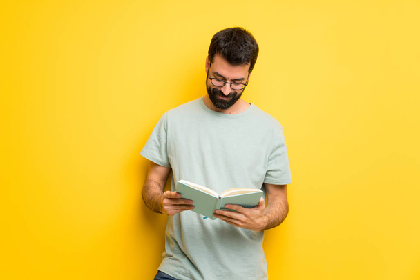 Mies, jolla on parta ja vihreä paita, pitää kirjaa ja nauttii lukemisesta
 - Valokuva, kuva
