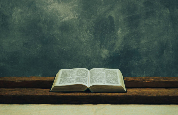 Bibbia aperta su un vecchio tavolo. Bellissimo sfondo grigio muro. Concetto religioso
. - Foto, immagini