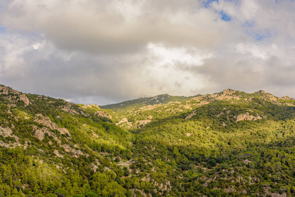 Kolor krajobraz na zewnątrz obraz formacji skalnej y mountainl na Sardynii, we Włoszech, z drzewami i wieże telekomunikacyjne na górze zrobione w pochmurny letni dzień - Zdjęcie, obraz