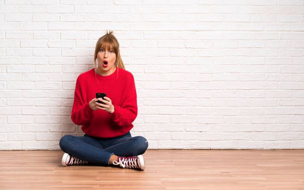 Punapää nainen istuu lattialla yllättynyt ja lähettää viestin
 - Valokuva, kuva