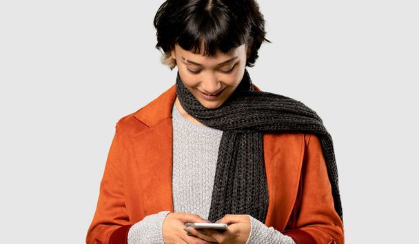 kurze Haare Frau mit Mantel sendet eine Nachricht mit dem Handy auf isoliertem grauen Hintergrund - Foto, Bild