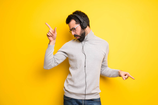 Hombre con barba y cuello alto escuchando música con auriculares y bailando
 - Foto, imagen