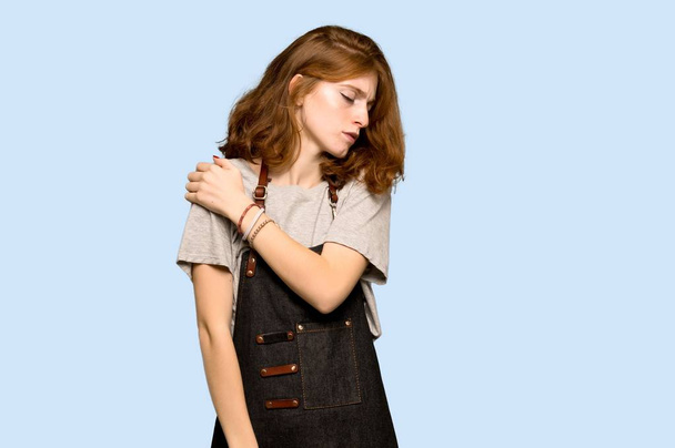 Young redhead woman with apron suffering from pain in shoulder for having made an effort over blue background - Foto, imagen