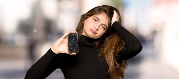 hübsches Mädchen mit kaputtem Handy im Freien - Foto, Bild