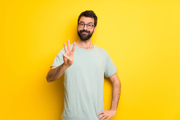 Mann mit Bart und grünem Hemd glücklich und zählt mit den Fingern drei - Foto, Bild