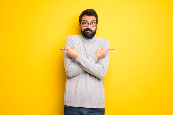 Man with beard and turtleneck pointing to the laterals having doubts - Foto, Imagen