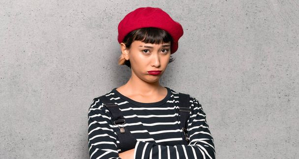 Young woman with beret with sad and depressed expression over textured wall - Фото, зображення