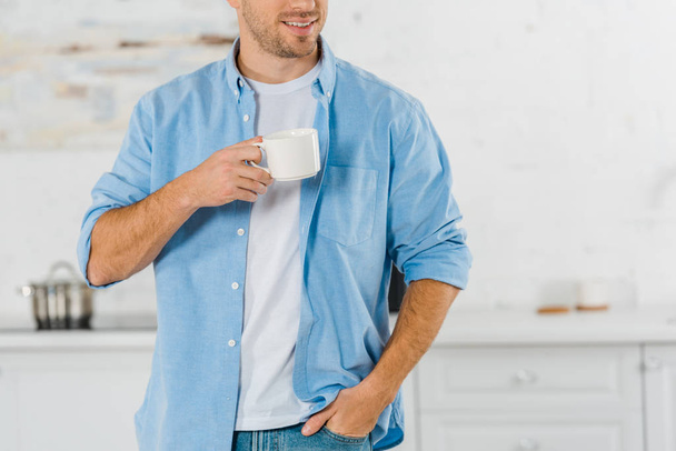 cropped view of smiling man in casual clothes drinking coffee in kitchen - 写真・画像