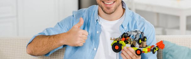 evde oyuncak araba ve tabela gösteren başparmak tutarak gülümseyen adam görünümünü kırpılmış - Fotoğraf, Görsel