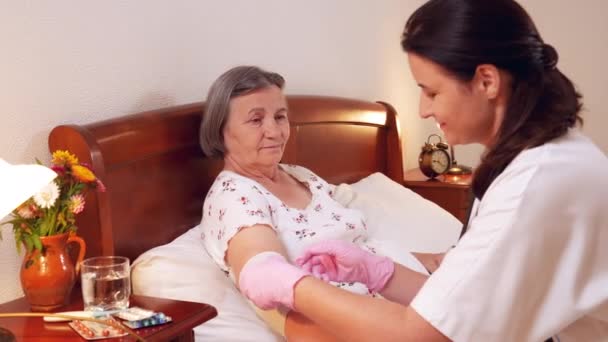 Vrouwelijke arts verbanden senior vrouw elleboog thuis. Geneeskunde, leeftijd, ondersteuning, gezondheidszorg en mensen concept - dokter zorgzame senior patiënt. Slow motion 4k - Video