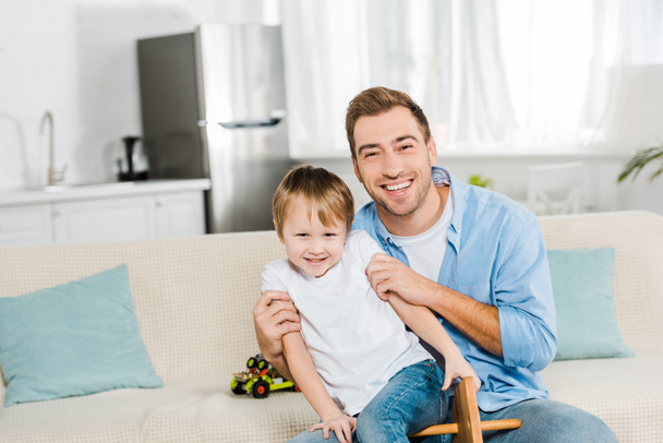 happy father hugging son and looking at camera at home - Fotoğraf, Görsel