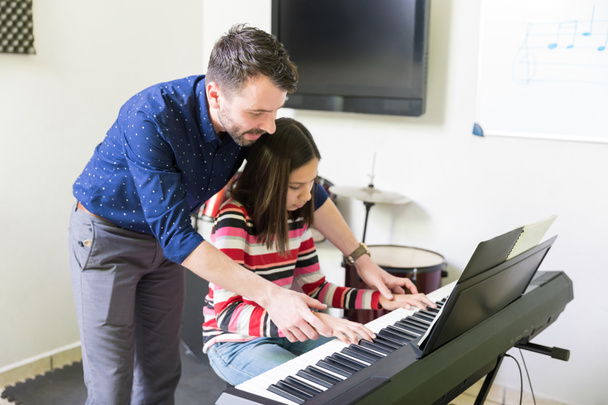 Music teacher guiding teen student to play electric instrument at classroom - Foto, afbeelding