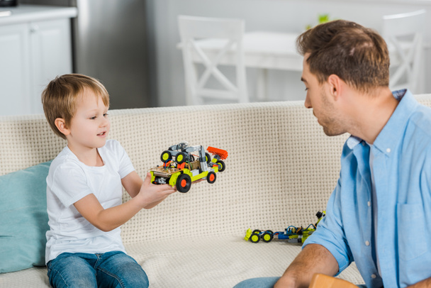 adorable preschooler son showing toy car to father at home - Foto, Imagen