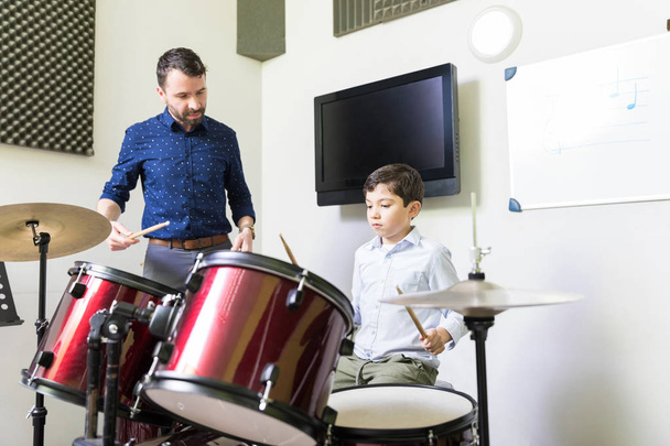 Profesor masculino guiando a niño pequeño en tutorial de aprendizaje de tambor en la academia de música
 - Foto, imagen