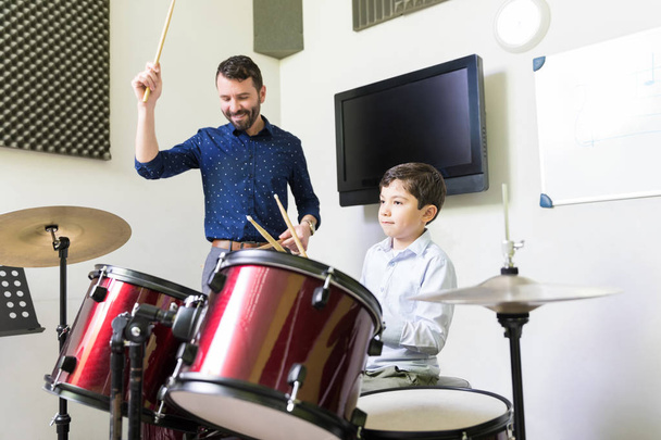 Instructor sonriente tocando la batería con el estudiante durante la clase de música
 - Foto, Imagen