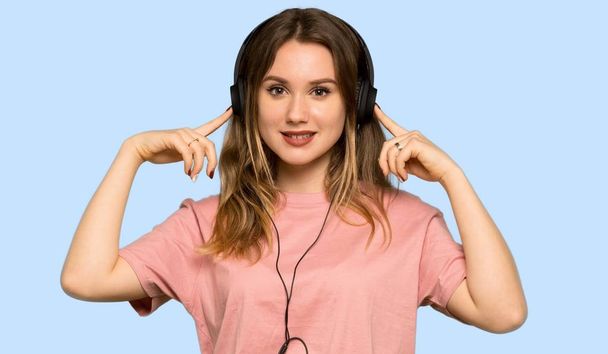 Adolescente avec pull rose écoutant de la musique avec écouteurs sur fond bleu isolé
 - Photo, image