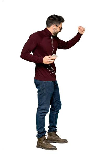 Full-length shot of Handsome man with glasses listening music with the phone on isolated white background - Fotó, kép