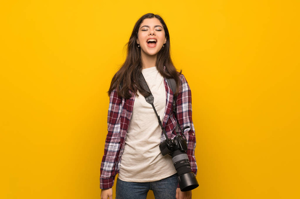 Fotograaf tiener meisje over gele muur schreeuwen aan de voorkant met de mond wijd open - Foto, afbeelding