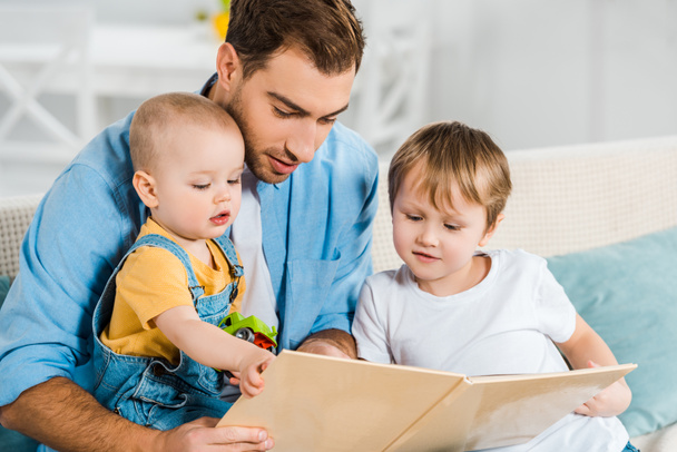 幼児および幼児の息子自宅に本の座っているハンサムな父親と読書 - 写真・画像