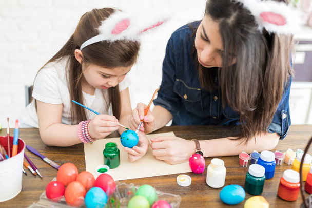 Äiti ja lapsi käyttävät siveltimiä munien maalaamiseen pääsiäisenä kotona
 - Valokuva, kuva