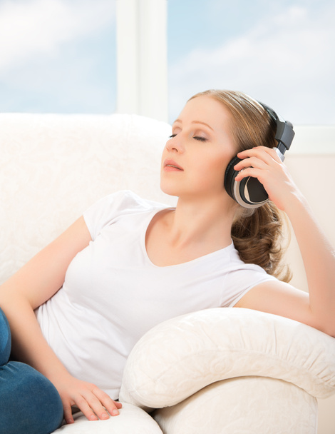 Frau mit Kopfhörer genießt Musik, während sie zu Hause auf dem Sofa liegt - Foto, Bild