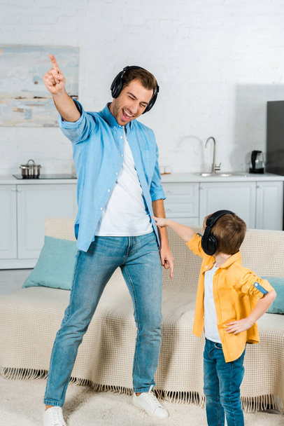 happy father with preschooler son in headphones listening music and pointing with fingers at home  - Fotografie, Obrázek