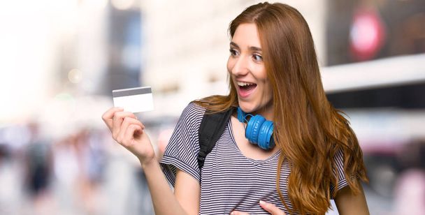 Redhead student woman holding a credit card and surprised in the city - Zdjęcie, obraz